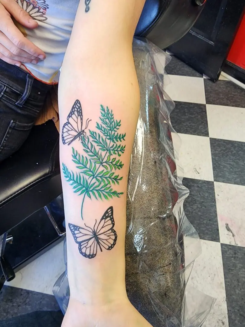 Two butterflies with a green tree as an arm tattoo